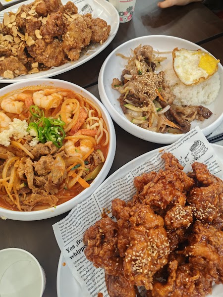A table filled with multiple plates of Asian-style fried chicken, stir-fried beef with rice, and a noodle dish with shrimp.
