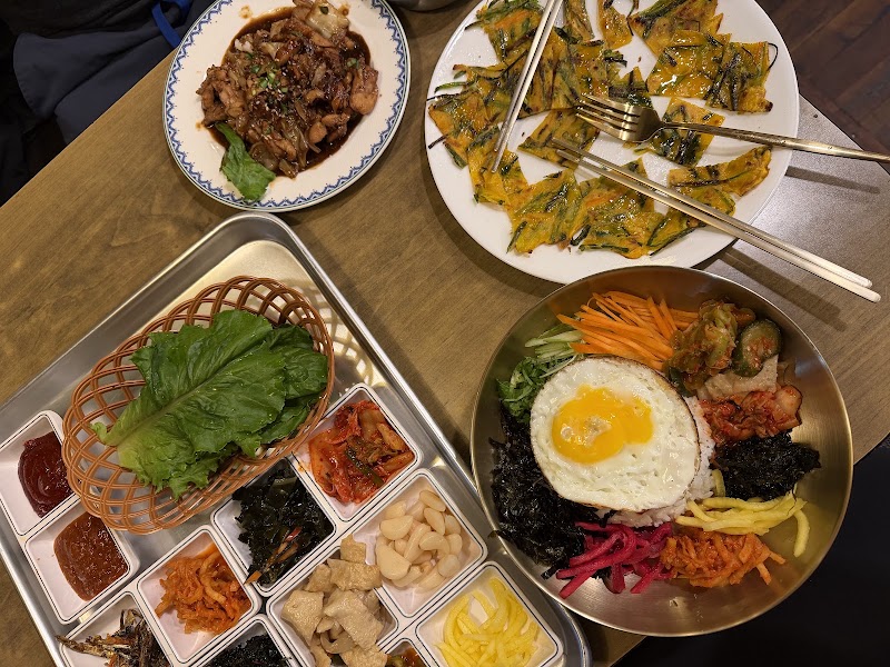 Table spread with bibimbap bowl topped with fried egg, scallion pancakes, and side dishes