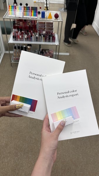 Two hands hold personal color analysis report booklets in a studio with makeup shelves.