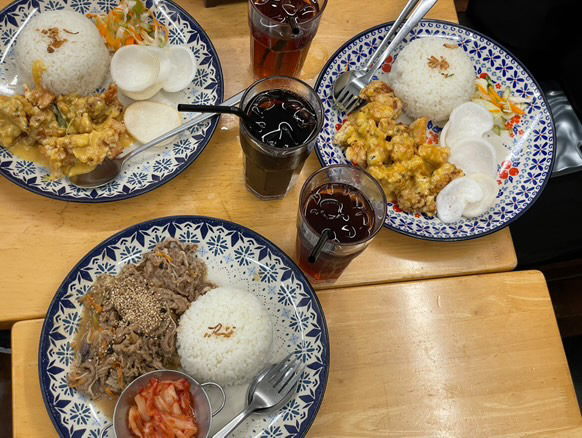 Three plates of Southeast Asian and Korean style dishes on a restaurant wooden table.