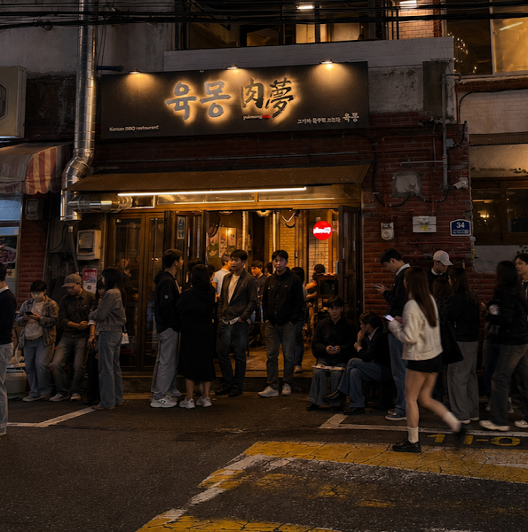 Exterior of Yookmong Korean BBQ restaurant in Seoul at night with a crowd of people waiting outside.