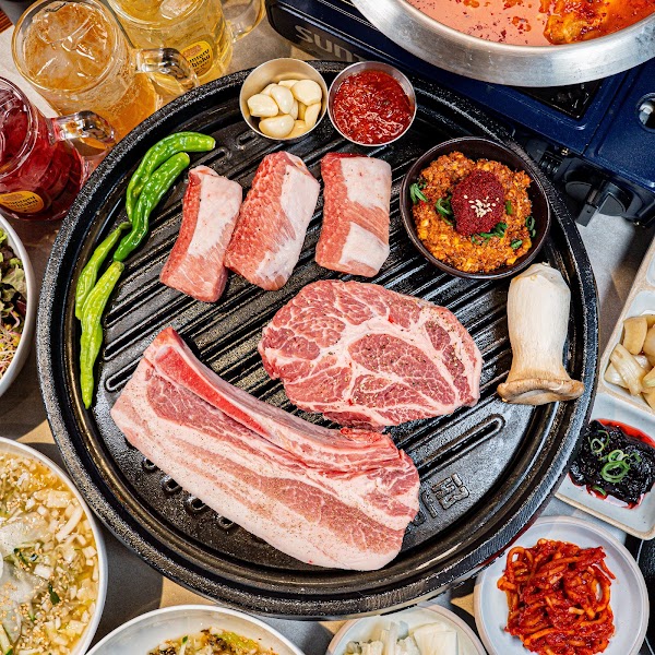 Pork cuts, fresh garlic, chili paste, and side dishes arranged for barbecue