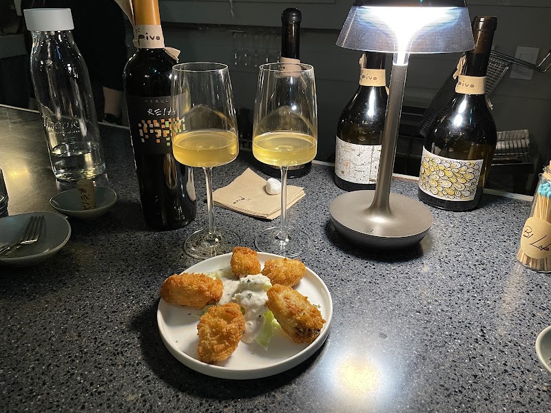 Two glasses of white wine and a plate of fried food on a dark granite bar top