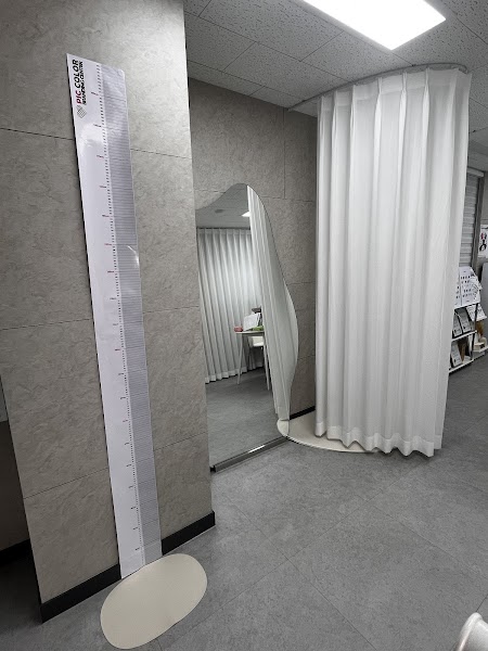 A professional consultation studio interior featuring a height measuring chart, an asymmetrical standing mirror, and a white privacy curtain.