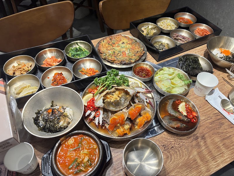 Top-down view of a Korean feast with a variety of side dishes, soy-marinated crab, a savory pancake, and soup on a wooden table.