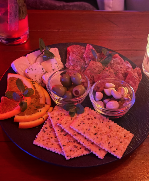 Charcuterie plate with cheese, crackers, olives, nuts, and orange slices under ambient lighting