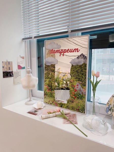 A framed decorative poster with the word damppeum sitting on a window sill with small artificial flowers and a mannequin bust