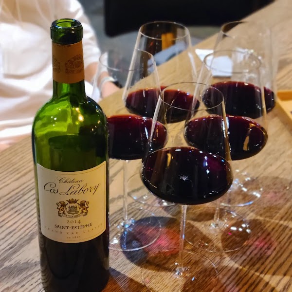 Bottle of Château Cos Labory Saint-Estèphe red wine surrounded by crystal glasses on a wooden table