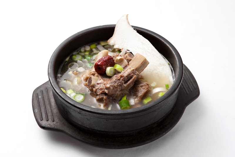 A bowl of Galbitang Korean beef short rib soup served in a traditional black earthenware pot on a white background.