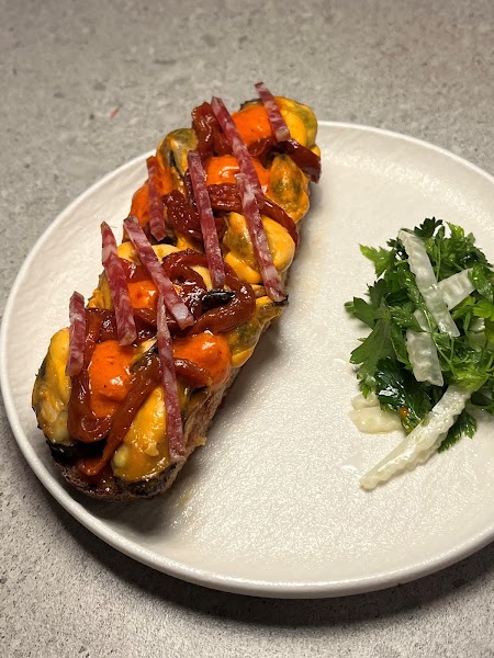 Gourmet toasted bread topped with mussels, roasted peppers, and thin cured meat