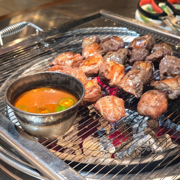 Cubed pork grilling on wire charcoal grill with warmed dipping sauce cup