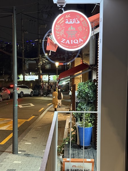 Illuminated circular street sign for Zaiqa Tandoori and Curry House on Usadan street at night