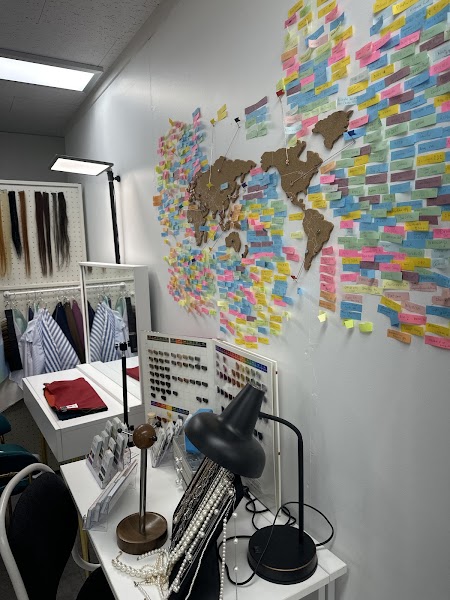 An office wall decorated with a cork world map and many colorful sticky notes, with a desk featuring jewelry and color samples.