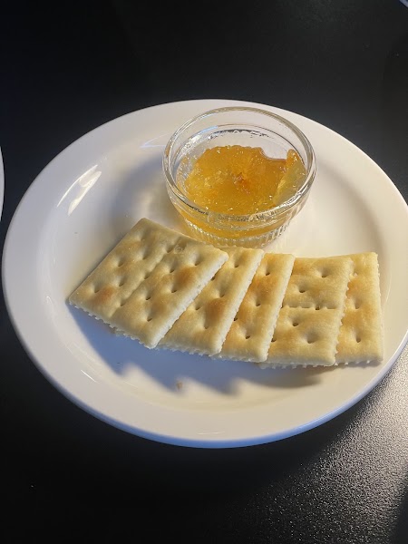 Small white plate containing saltine crackers and a small glass bowl of orange marmalade