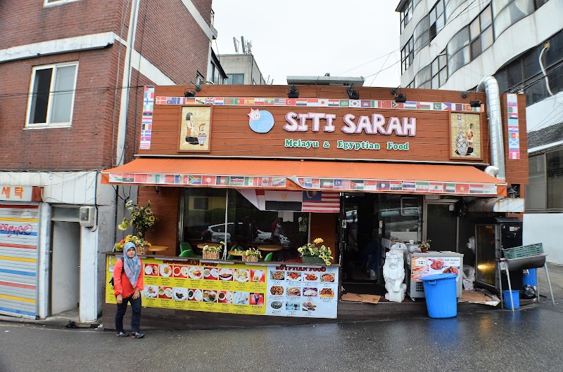Exterior view of Siti Sarah restaurant in Seoul featuring wooden facade, food menus, and international flags.
