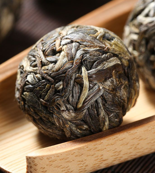 Close-up of a ball of compressed dried tea leaves resting on a bamboo tea scoop.
