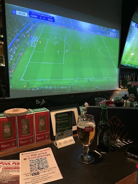 Large projector screen showing a live football match inside Liverpool Pub with draft glasses on the counter