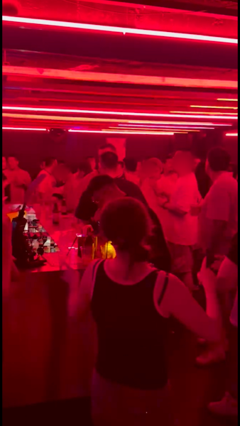 Crowd in a dimly lit bar with red neon light ceiling panels
