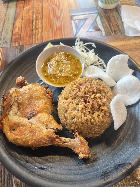 A plate of Indonesian fried chicken with rice, crackers, and spicy chili sauce