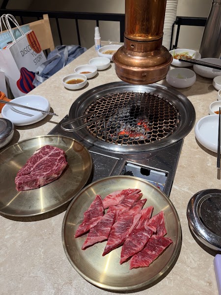 A Korean barbecue table set with raw beef slices, side dishes, and a charcoal grill vent