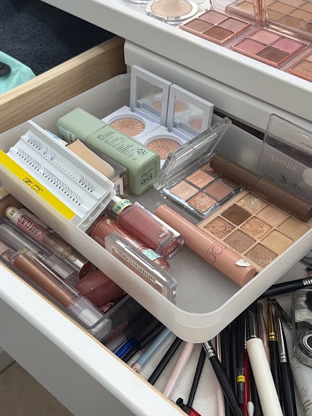 An open drawer filled with organized makeup products, eyeshadow palettes, and brushes.
