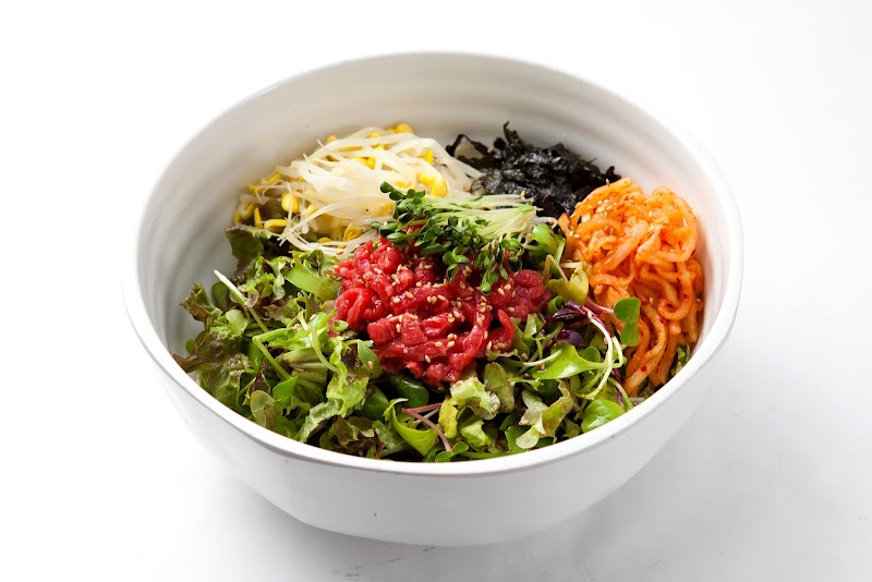 A white bowl containing yukhoe bibimbap with raw beef, greens, sprouts, and seasoned radish on a white background.