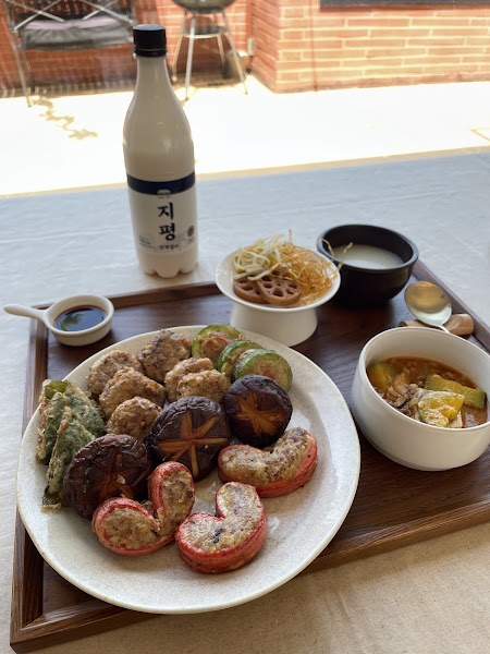 A wooden tray holding a plate of Korean pancakes, a bowl of stew, and a bottle of Makgeolli.