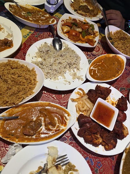 A flat-lay view of several plates filled with various Indian restaurant dishes including curries, rice, and tandoori meat
