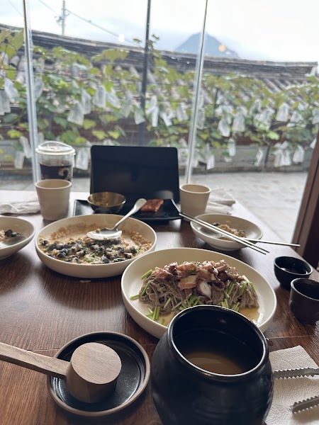 Dining table with fusion noodle dishes framed by a large window overlooking traditional tiled roofs