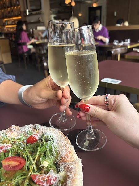 Two guests toasting sparkling wine flutes over pizza at Komfy Samgakji