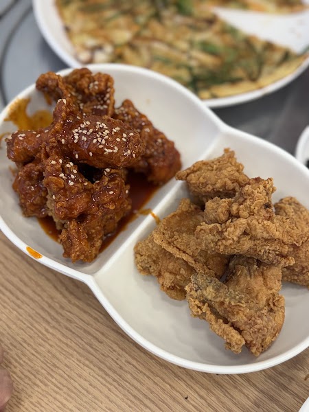 A split white bowl containing spicy glazed fried chicken and plain crispy fried chicken on a wooden table