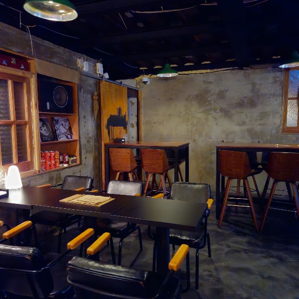 Dimly lit dining room with dark wooden tables, vinyl record shelf, and green pendant lights
