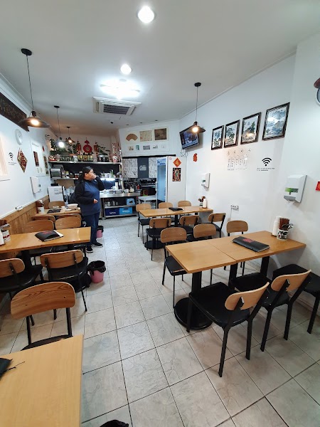 Interior view of a modest Chinese restaurant with wooden tables and black chairs.