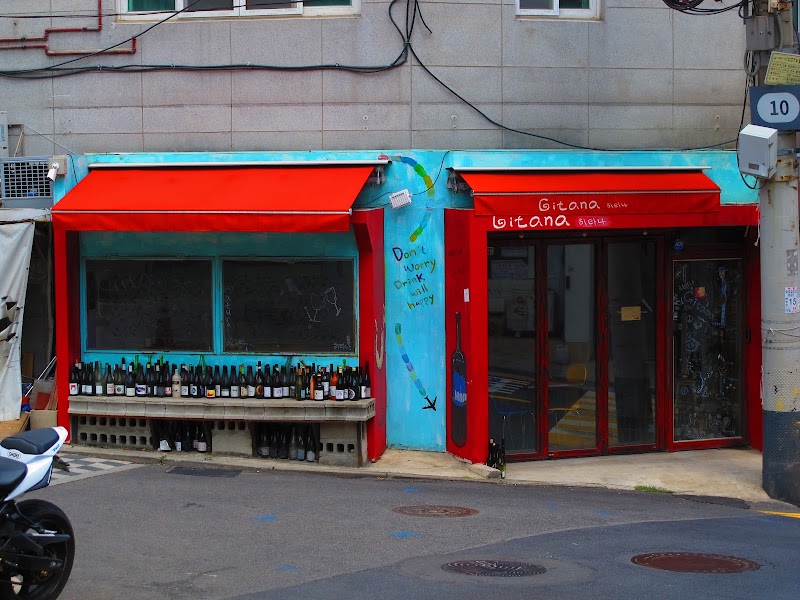 Vibrant turquoise storefront with red awnings and bottle bench at Gitana Natural Wine Bar