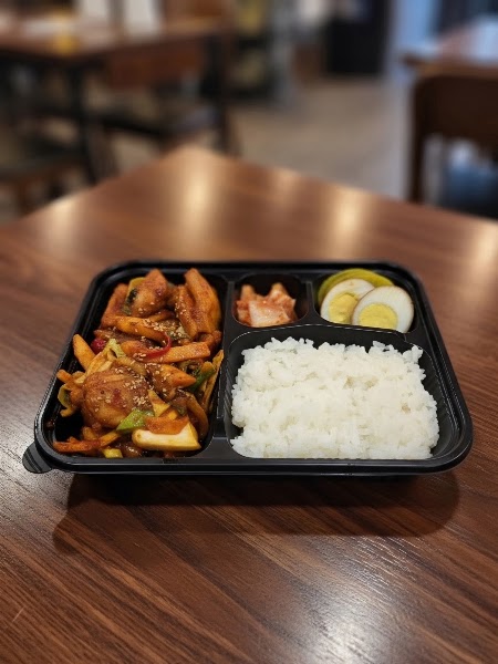 Partitioned Korean bento lunch container with stir-fried meat, rice, egg, and kimchi