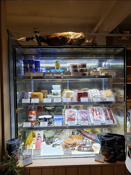 Refrigerated display case in the wine bar filled with whole cured jamón and packaged fine cheeses