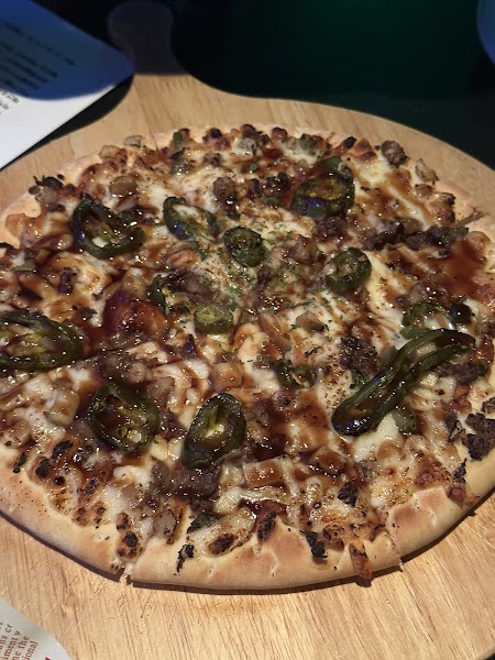 Thin-crust Bulgogi Pizza with green jalapeños and meat on a wooden serving board