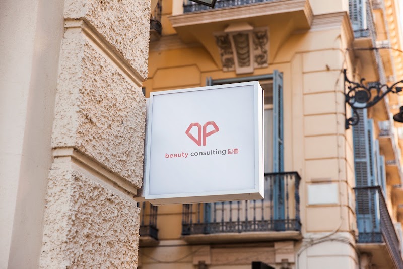 A square sign for a beauty consulting business attached to a textured beige wall with a classical building in the background