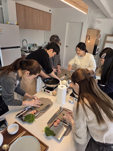 A group of people participating in an indoor Korean cooking class around a kitchen island.