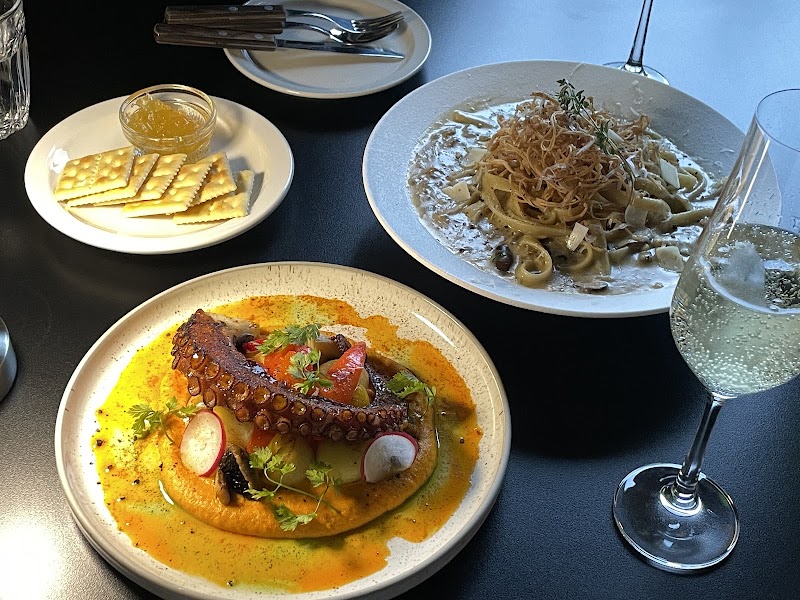 Grilled octopus, creamy pasta, crackers with jam, and a glass of sparkling wine on a black table