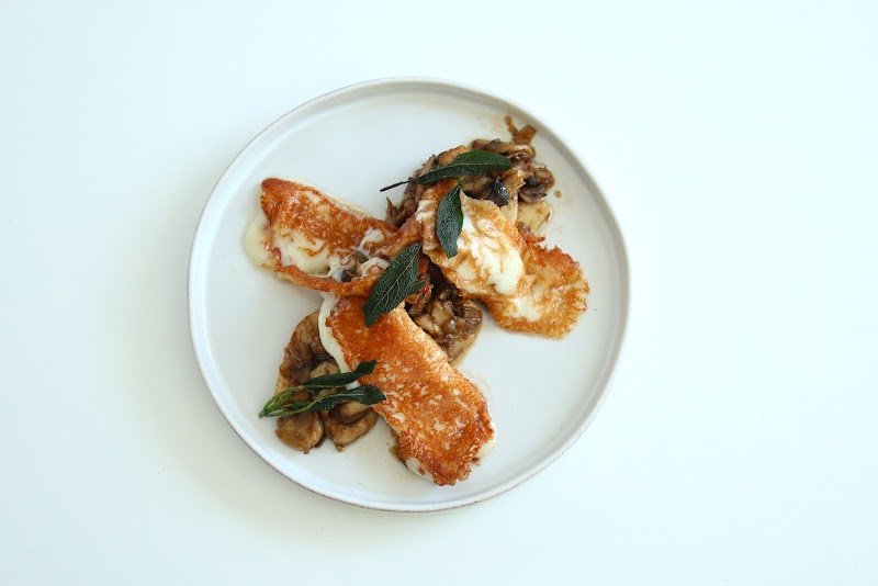 A plate of seared halloumi cheese and sautéed mushrooms garnished with fresh sage leaves