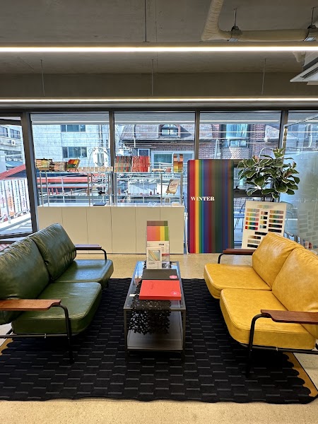 Interior of a color consulting studio featuring green and yellow leather sofas, a glass coffee table, and a color chart banner.