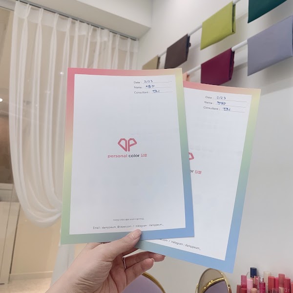 A person holding two personal color diagnosis result sheets in a bright studio