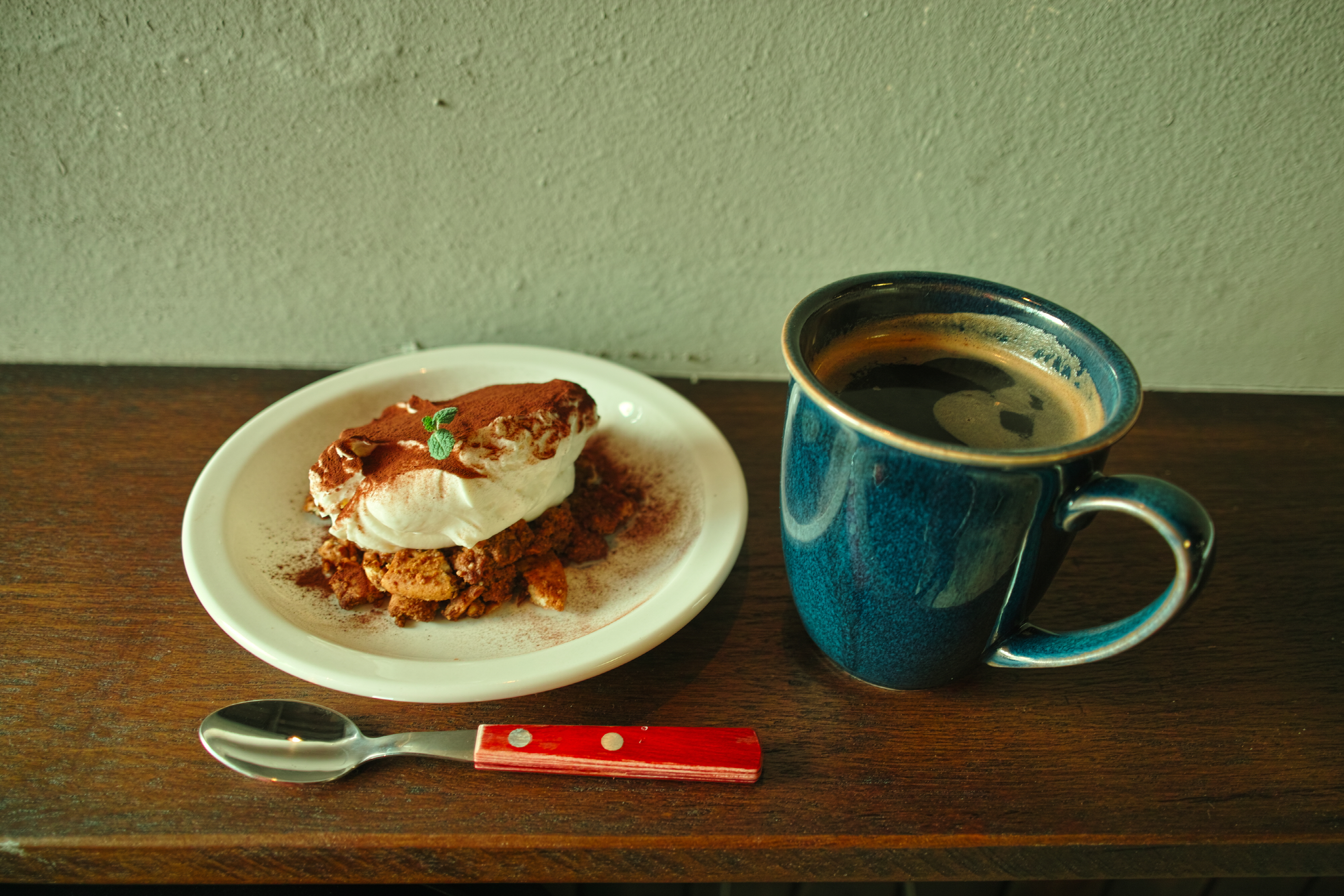 House tiramisu with cocoa powder alongside a dark blue coffee mug on a wooden table.