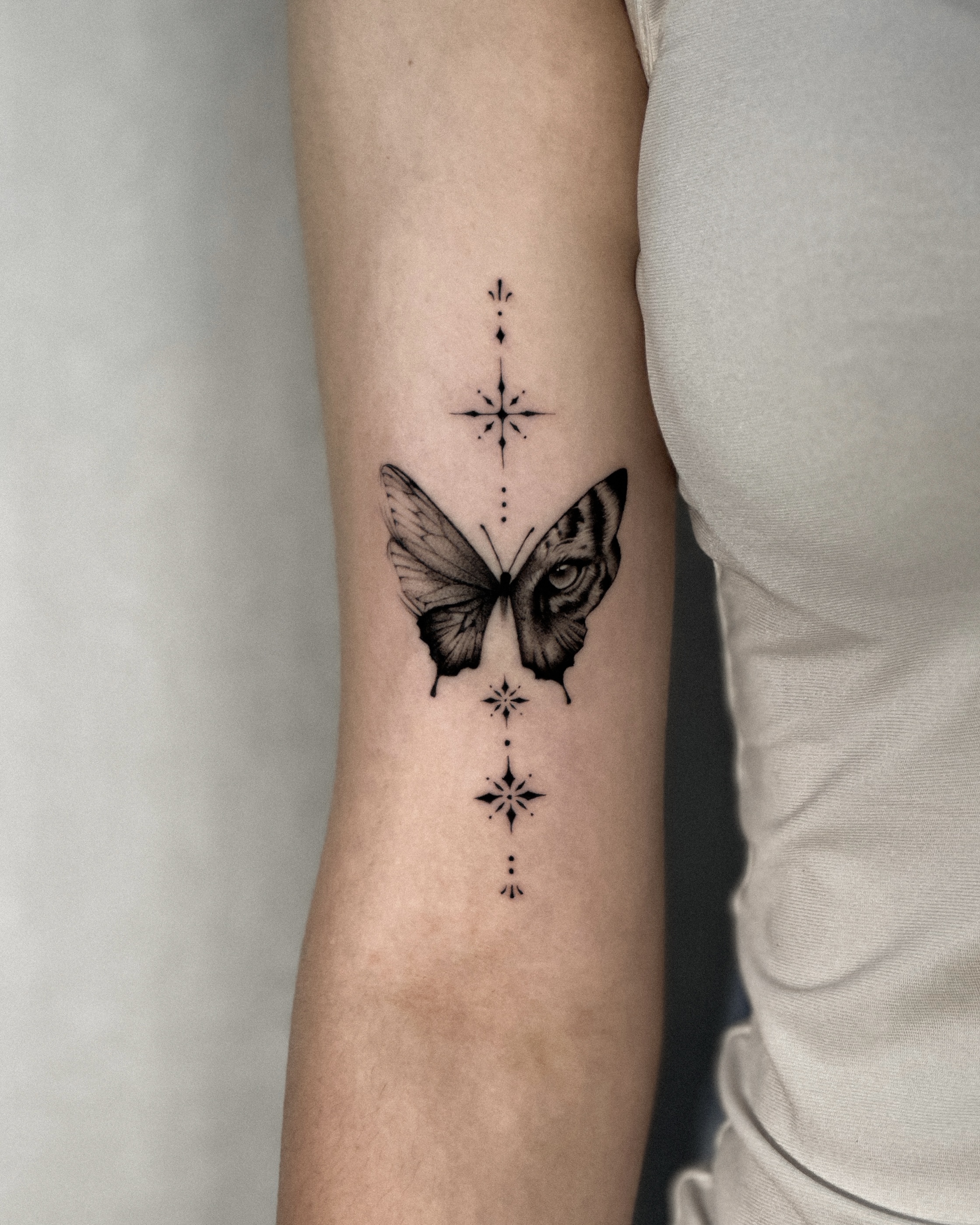 Fine-line tattoo on an upper arm featuring a butterfly with star motifs