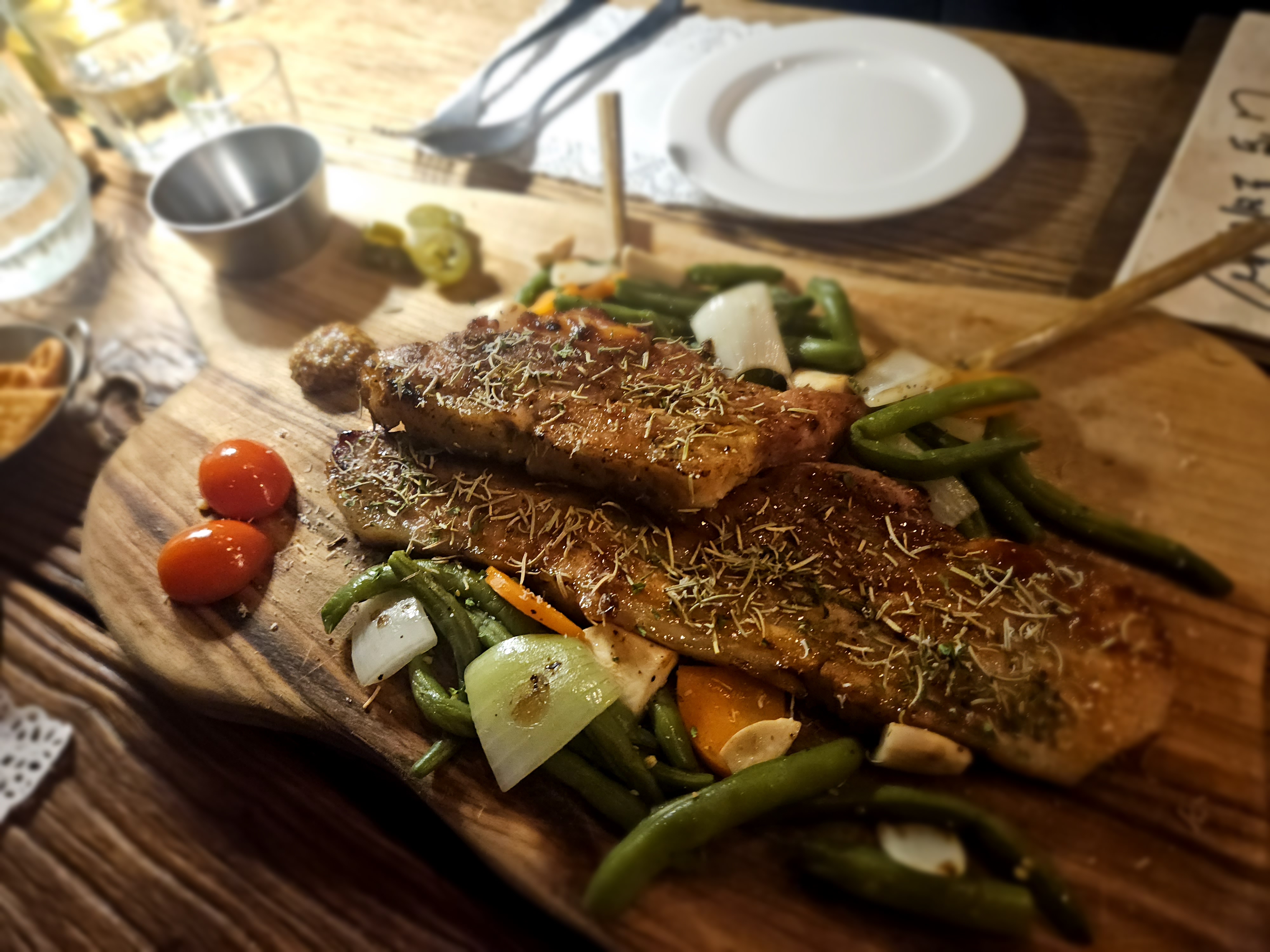 Seared grilled pork belly served on a wooden board with green beans, onions, and cherry tomatoes