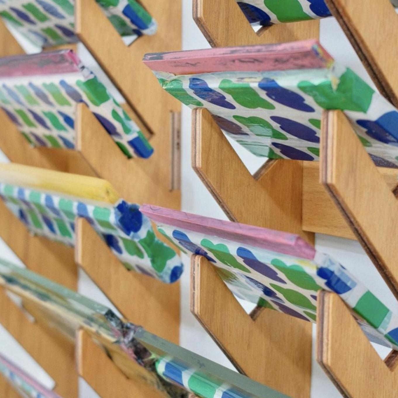 Close-up of screen printing squeegees with colorful patterned rubber blades resting on a wooden storage rack.