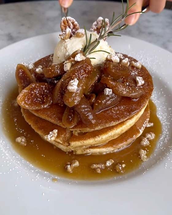 A stack of pancakes topped with figs, walnuts, and a scoop of cream on a white plate