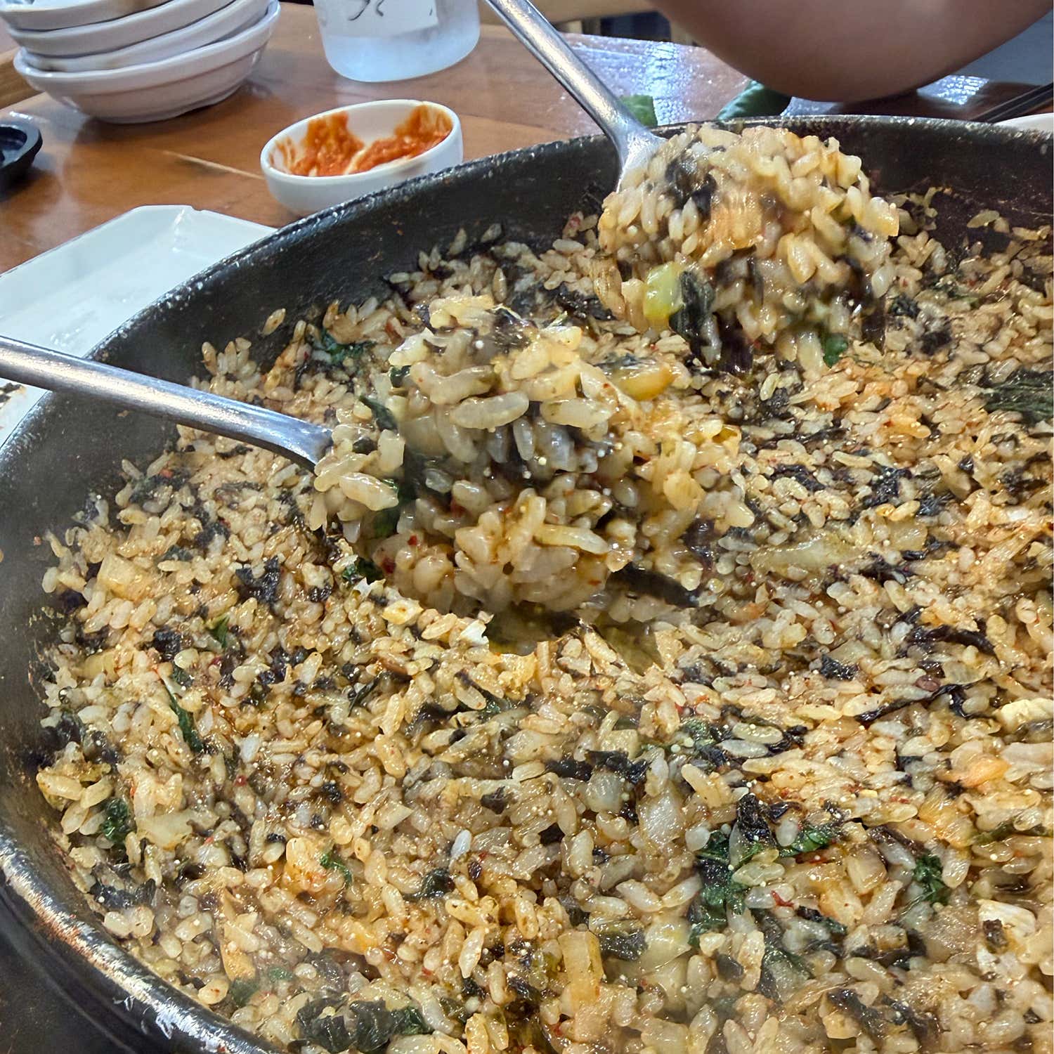 Close-up of fried rice mixed with vegetables in a large metal pan with two spoons lifting portions.