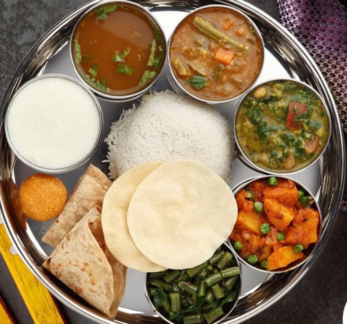 South Indian thali meal featuring steamed rice, vegetable curries, dal, yogurt, and flatbread on a metal tray